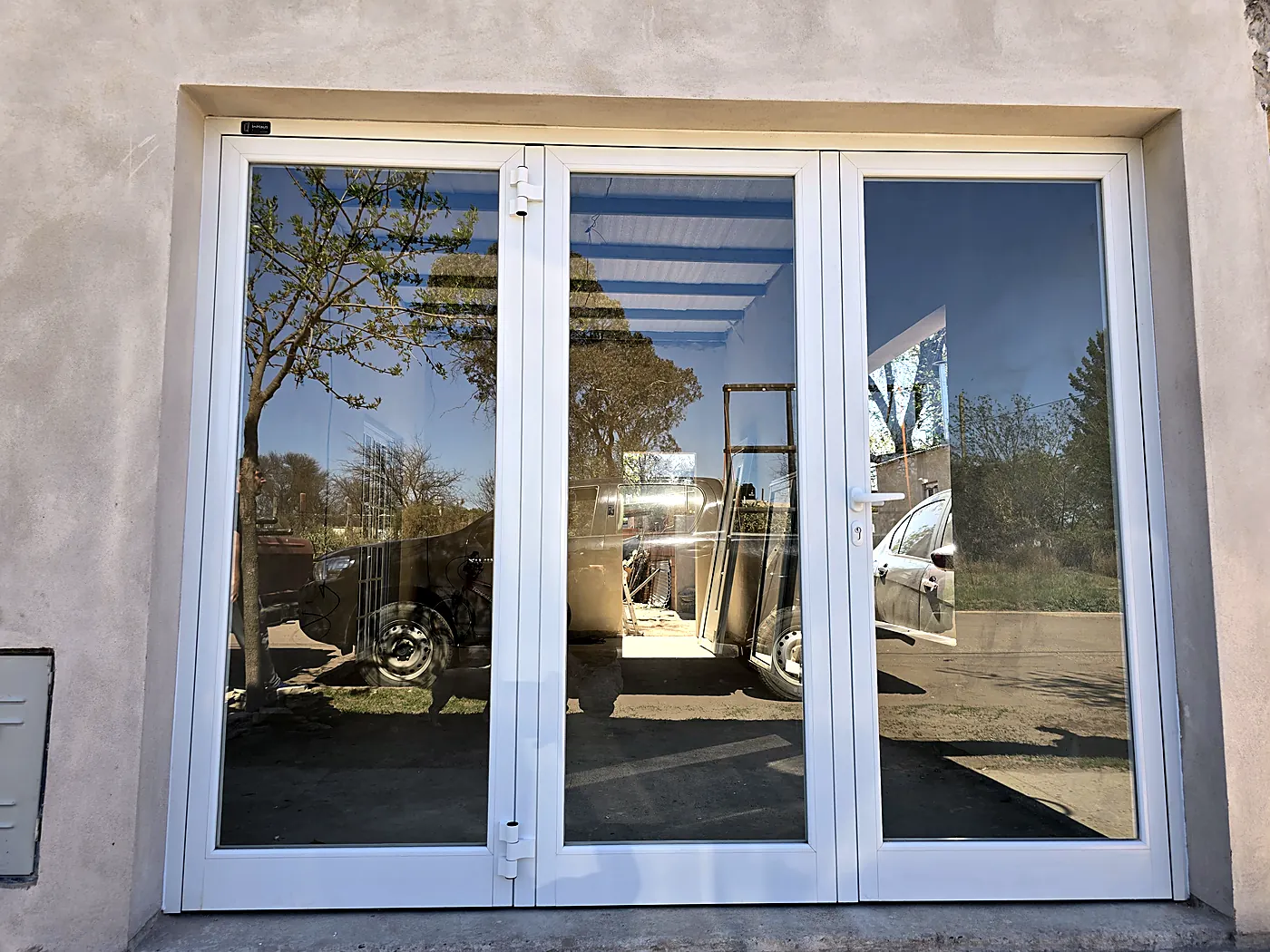 Portón de aluminio blanco vidriado, línea Módena, de tres hojas, en una fachada revocada