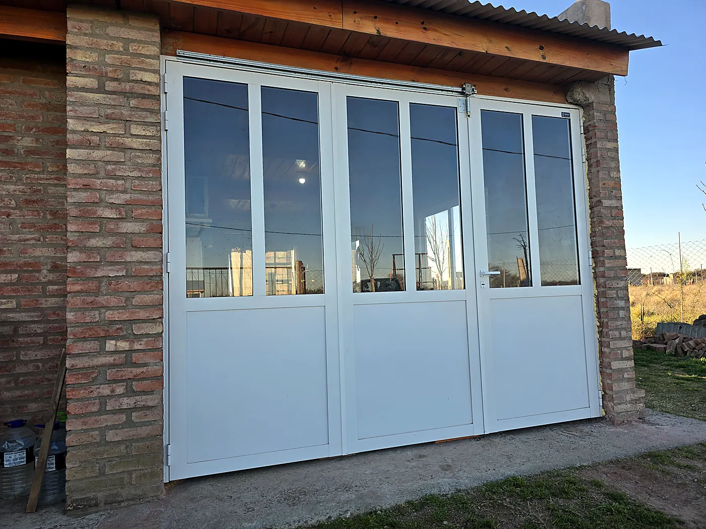 Portón de aluminio blanco de cuatro hojas con vidrios arriba, en una casa de ladrillo