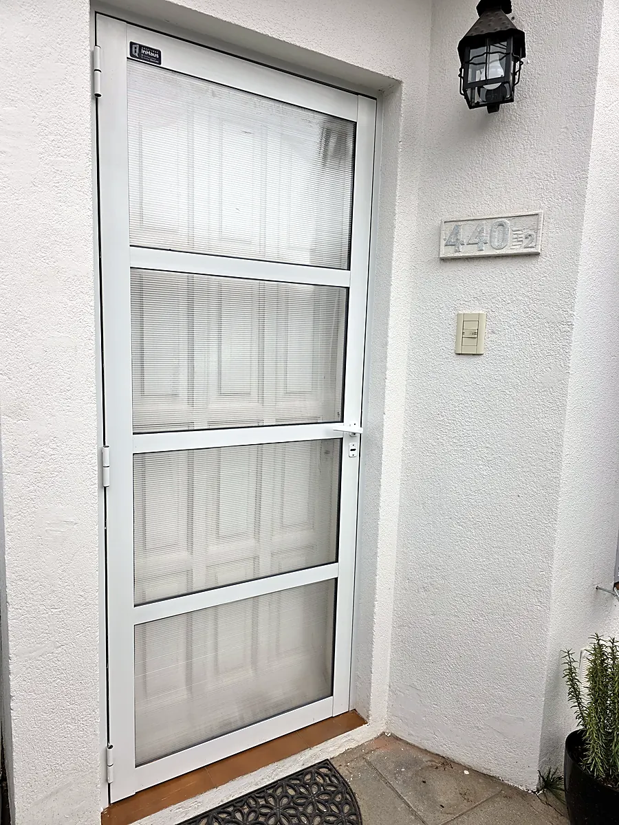 Puerta protectora de entrada de aluminio blanco, de cuatro paños con policarbonato alveolar