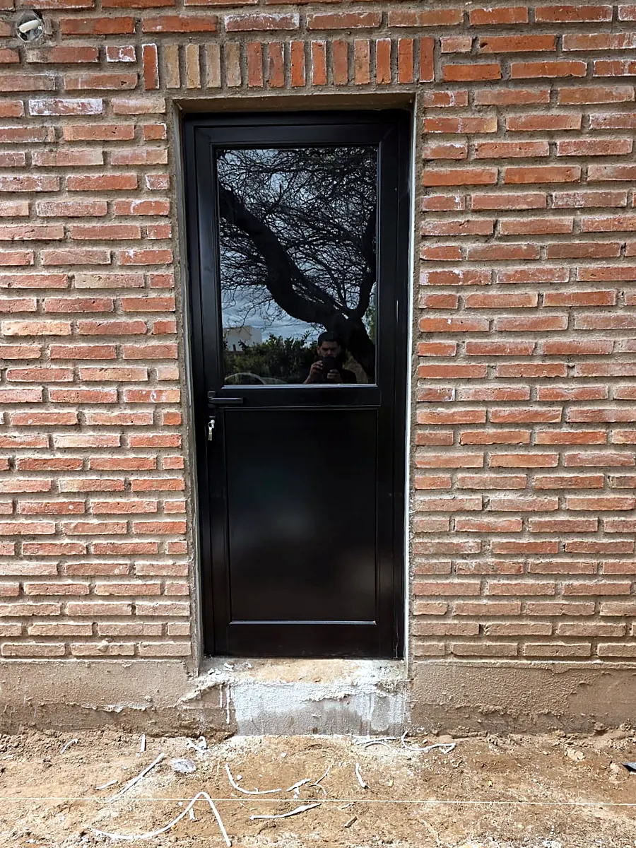 Puerta de aluminio negro con medio vidrio, recién colocada en una pared de ladrillo visto