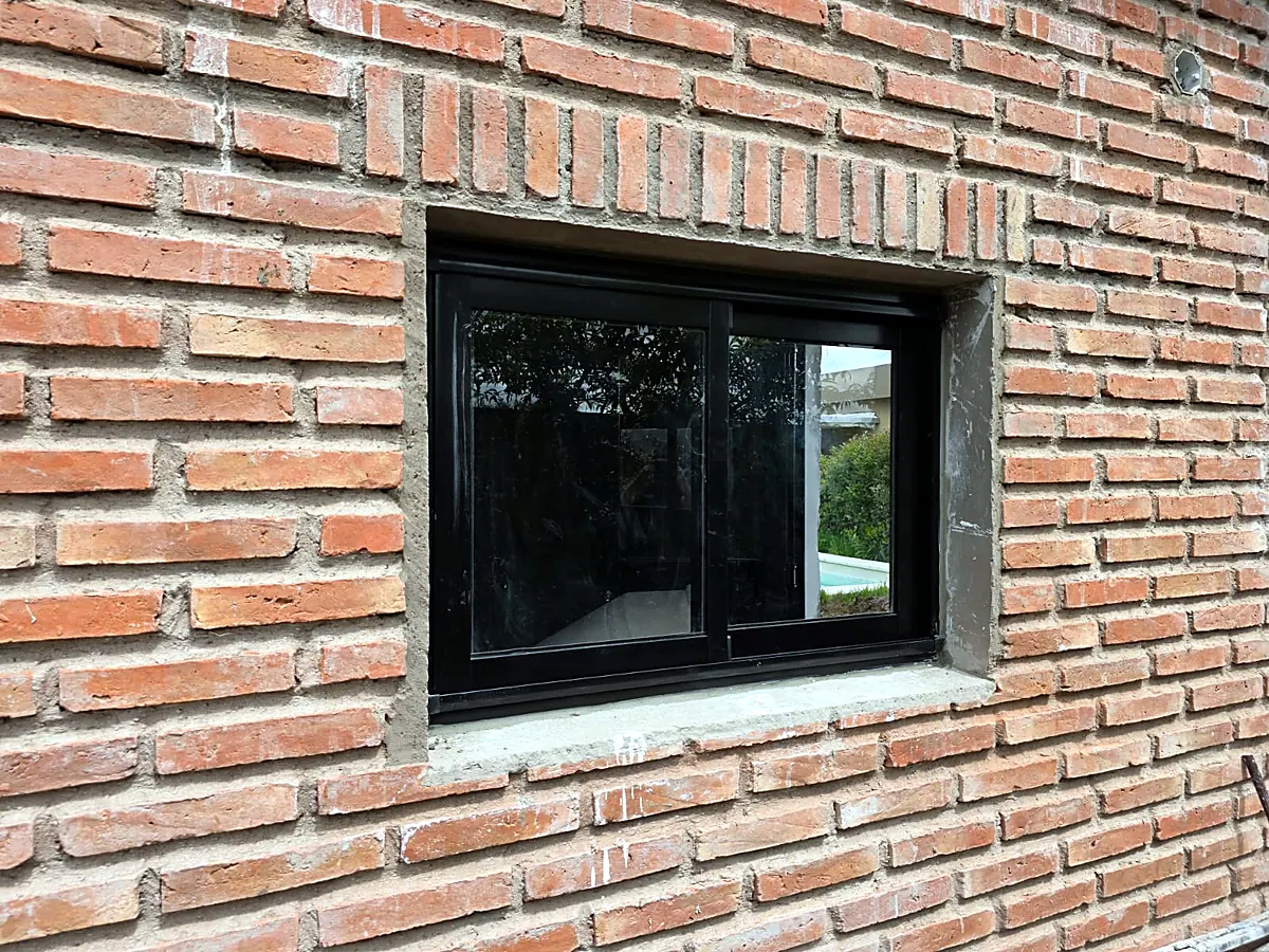 Ventana corrediza de aluminio negro en una pared de ladrillo visto