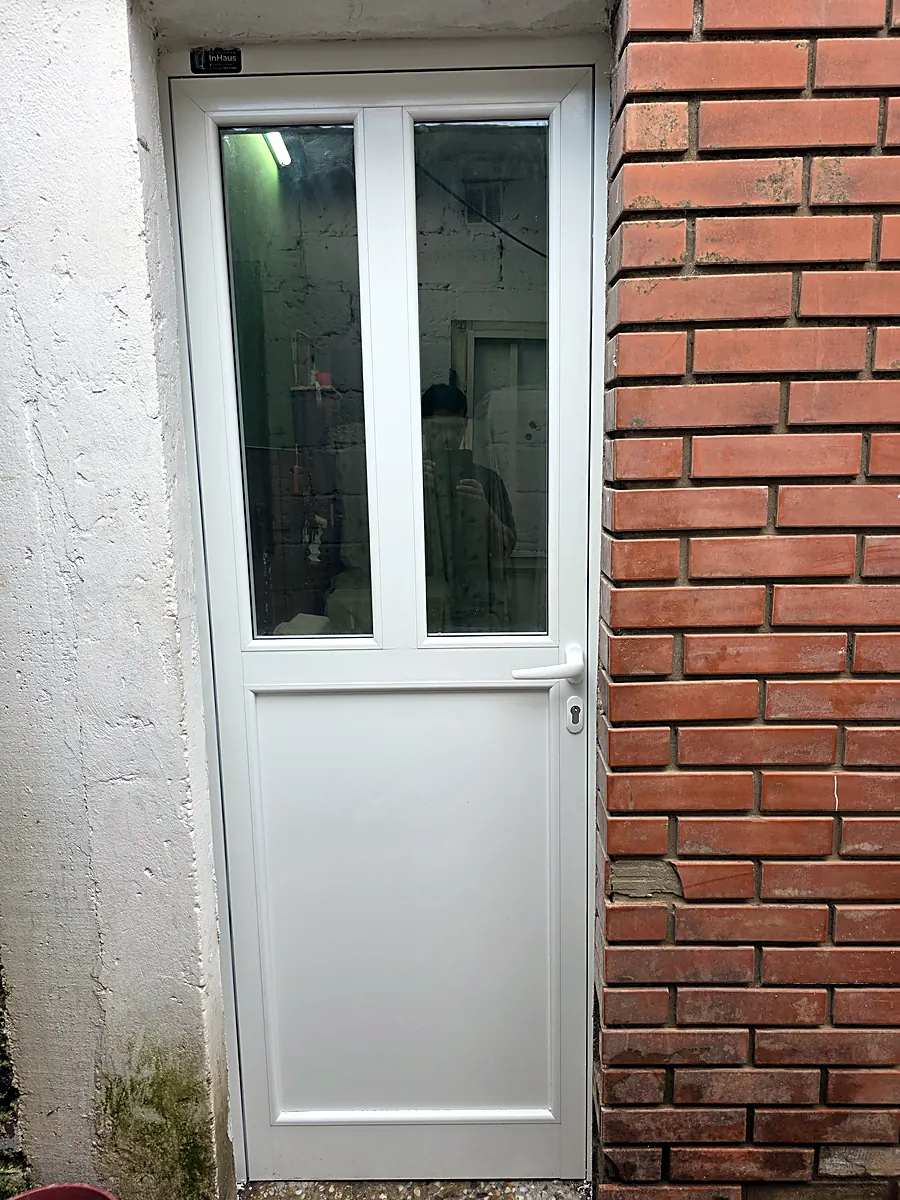 Puerta de servicio de aluminio blanco junto a una pared de ladrillo