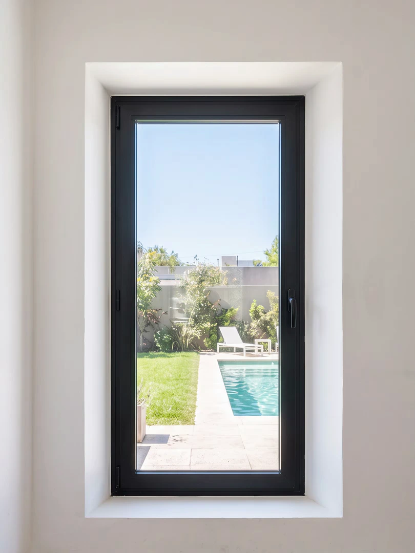 Ventana oscilobatiente de aluminio negro, cerrada, frente a un patio con pileta en verano